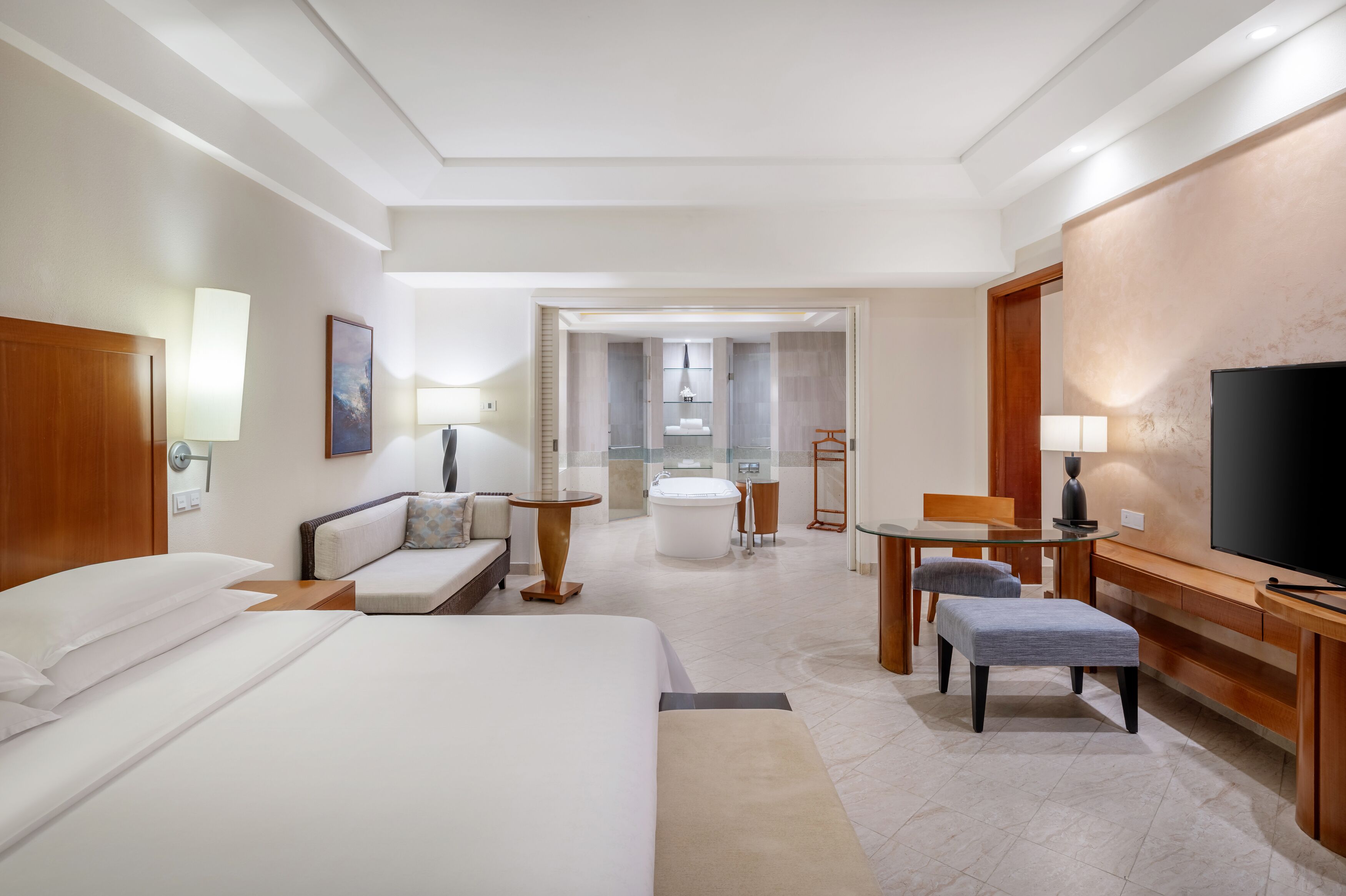 Une chambre d’hôtel avec un lit, un canapé, une télévision, un bureau et une salle de bain visible à travers une porte ouverte.