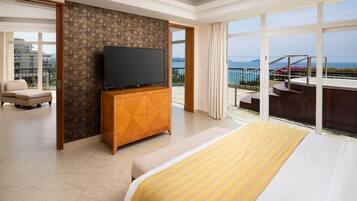 A hotel room with a large bed, a TV on a wooden cabinet, a balcony with a pool, and a view of the sea.