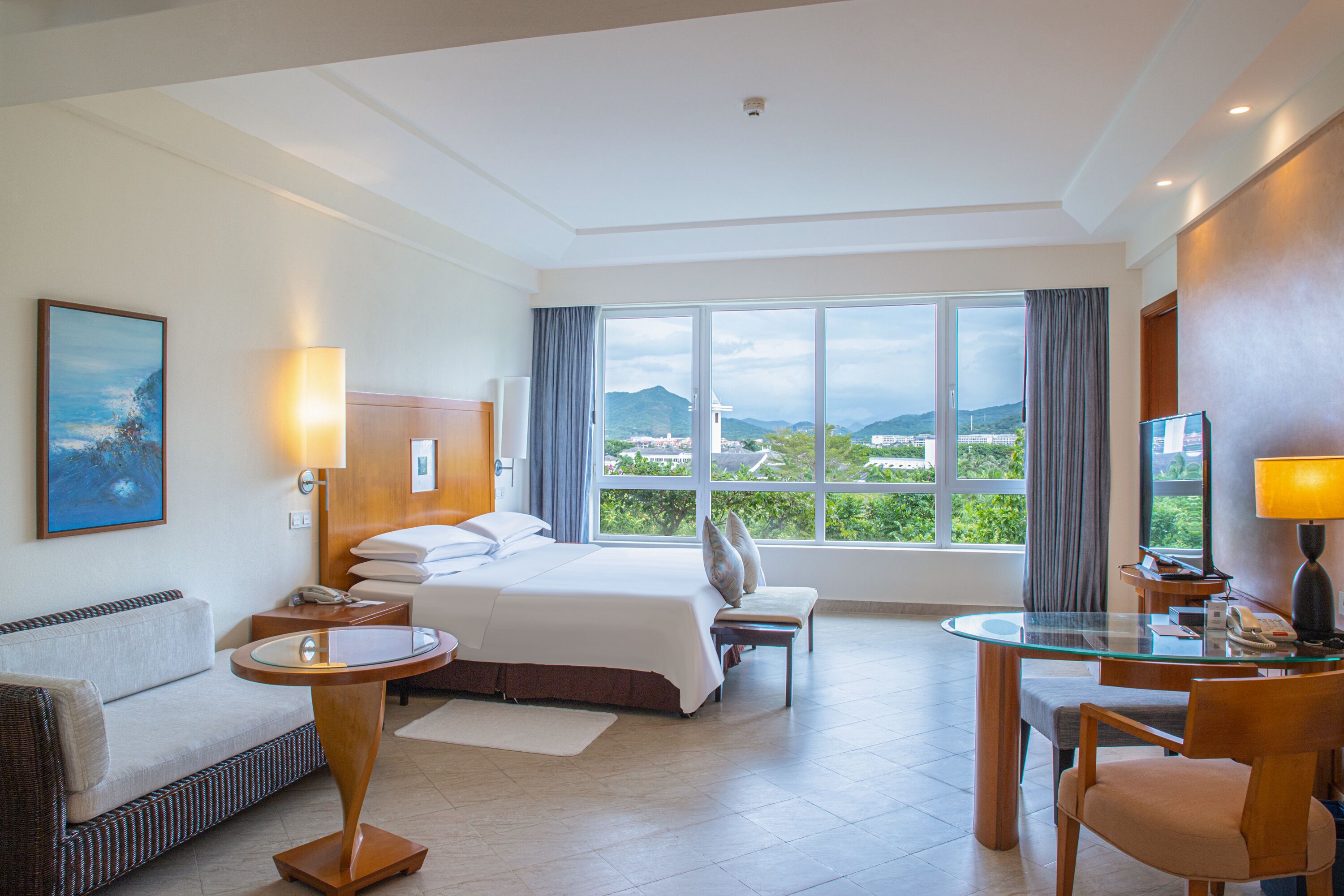 Habitación de hotel con cama, zona de estar con mesa y sillas, televisor y ventana grande que ofrece vistas al exterior.
