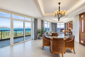 Amplia habitación con balcón y vista panorámica al océano, que cuenta con un comedor con mobiliario de mimbre y una lámpara moderna.