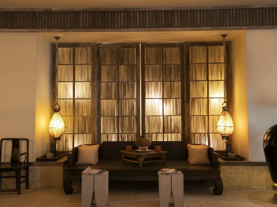 A room with a sofa, two chairs, a table with a vase, and two wall-mounted lamps.