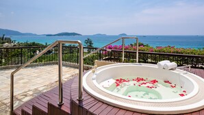 Un jacuzzi en una terraza de madera con barandilla, con vistas a una masa de agua y islas distantes.