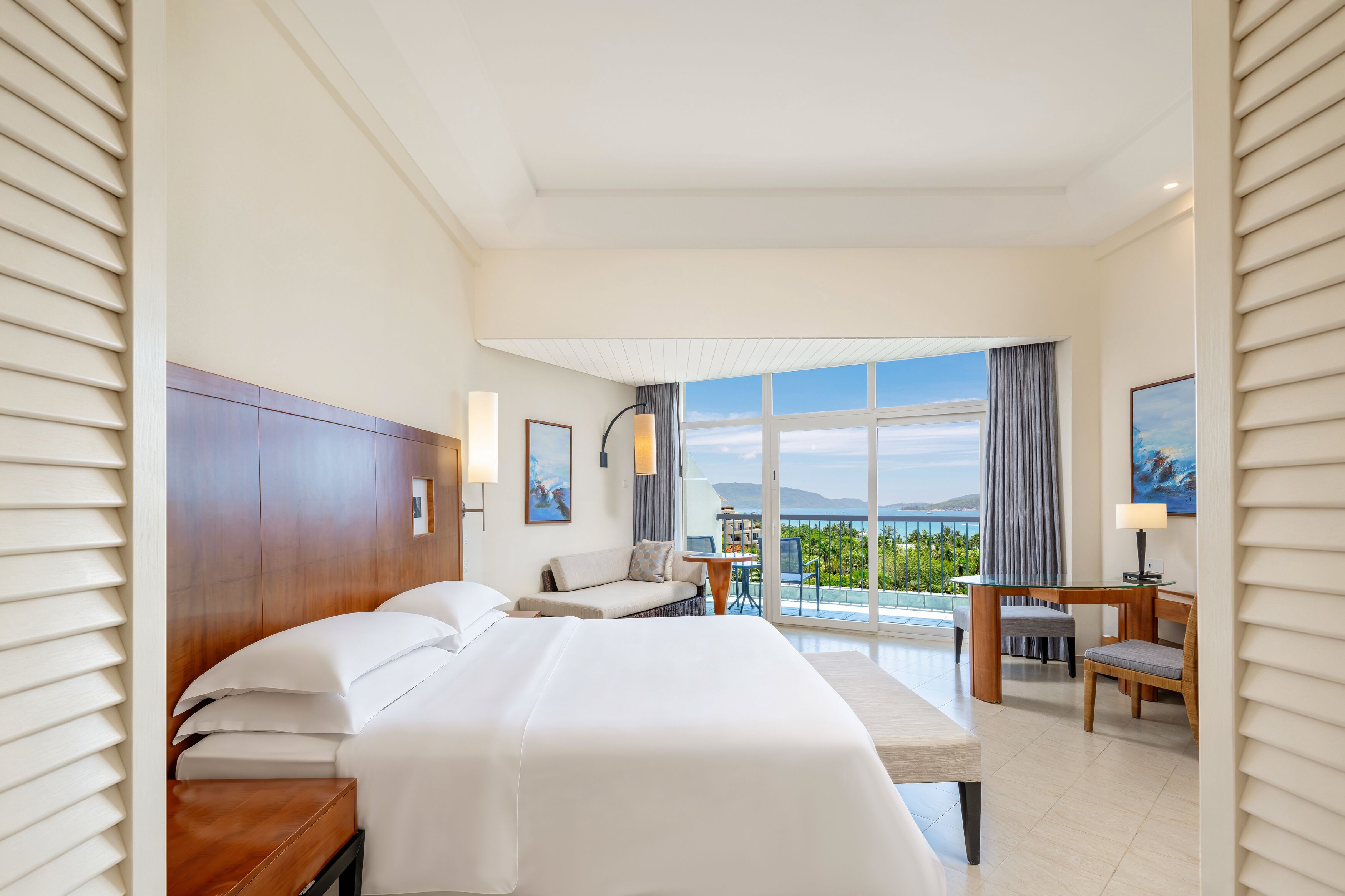 Een hotelkamer met een groot bed, een bureau, een stoel en uitzicht op zee.