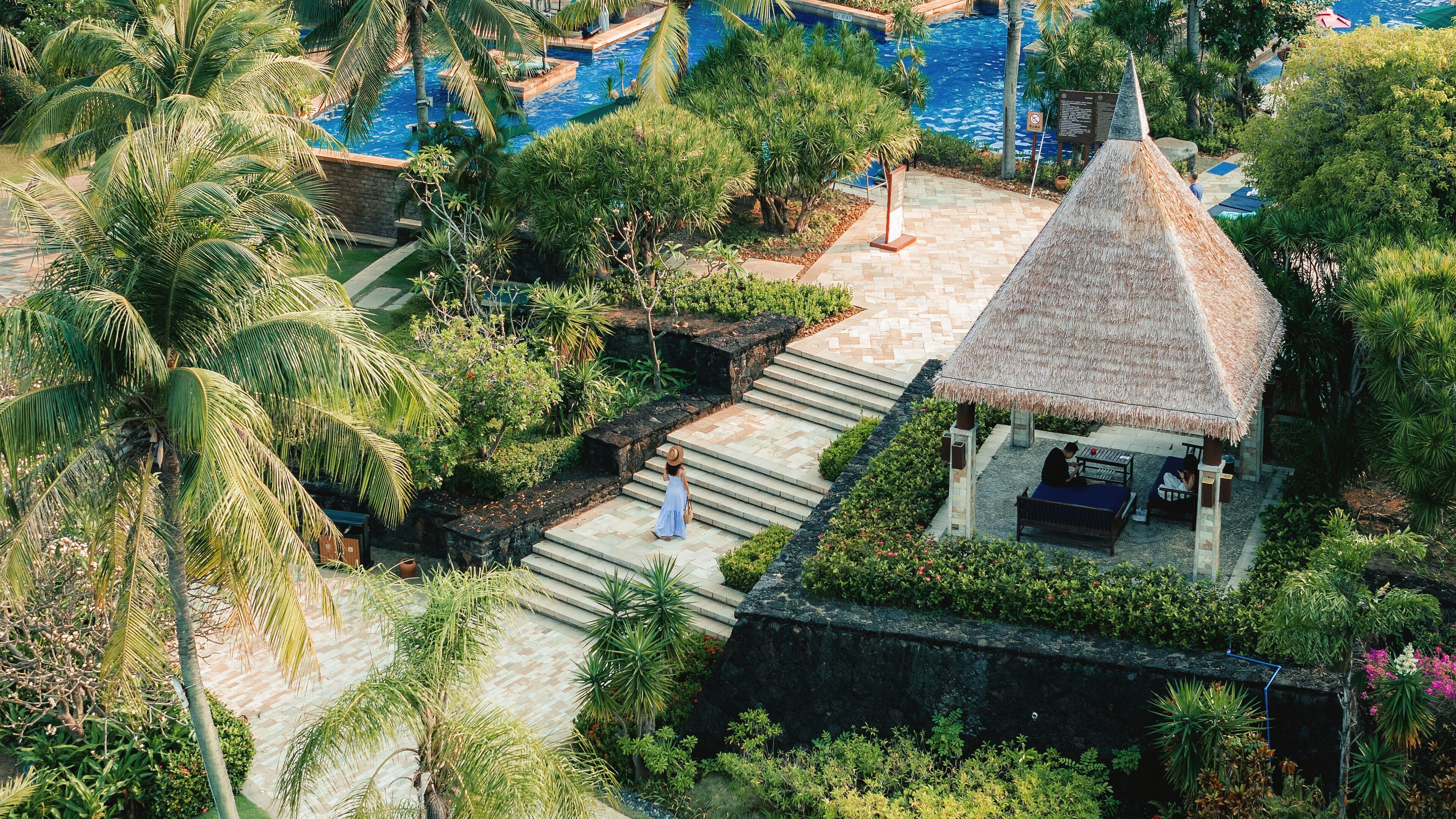 A resort with a swimming pool, palm trees, and a thatched-roof hut.