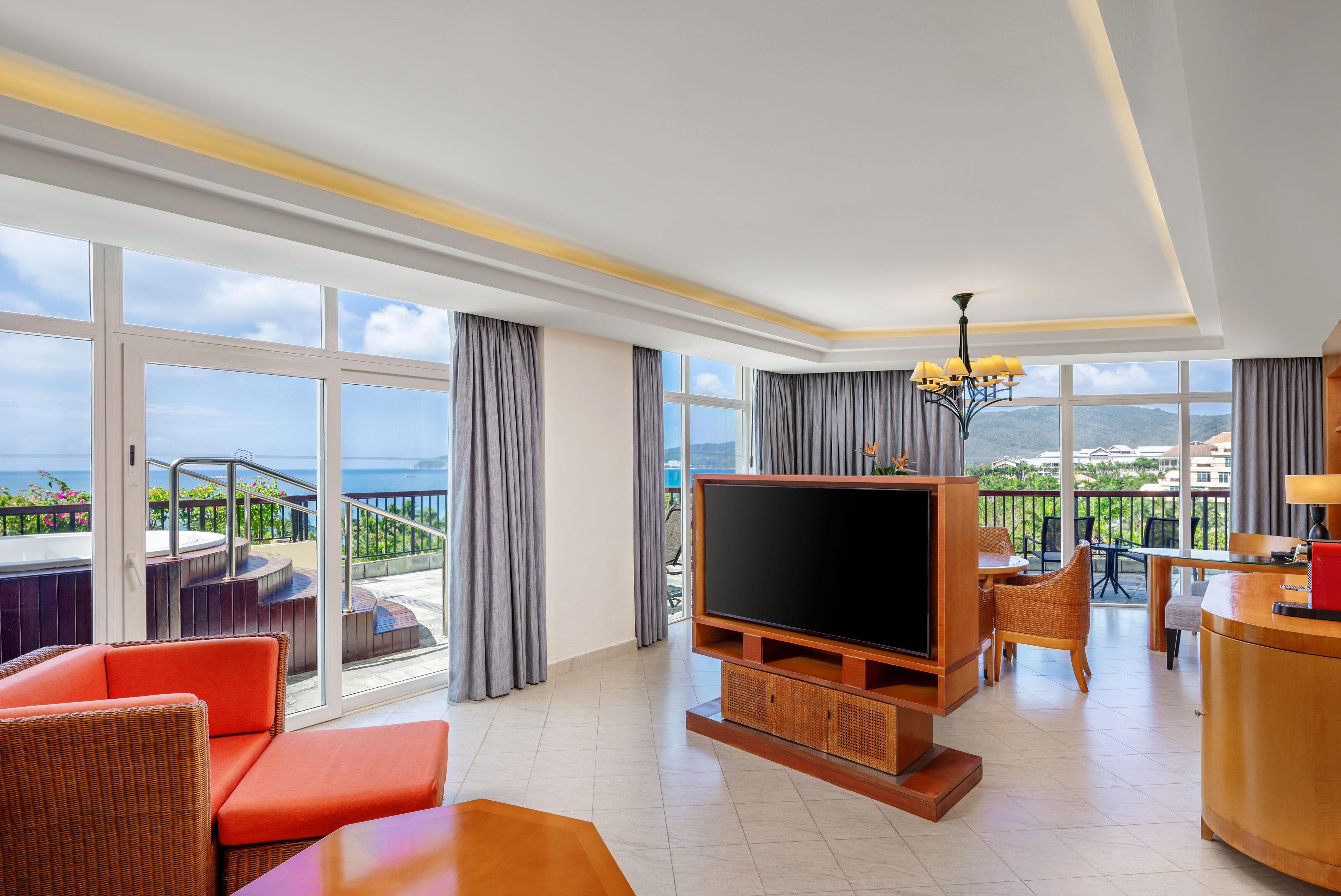 A hotel room with a large TV, wicker furniture, a balcony with a view, and a dining area.