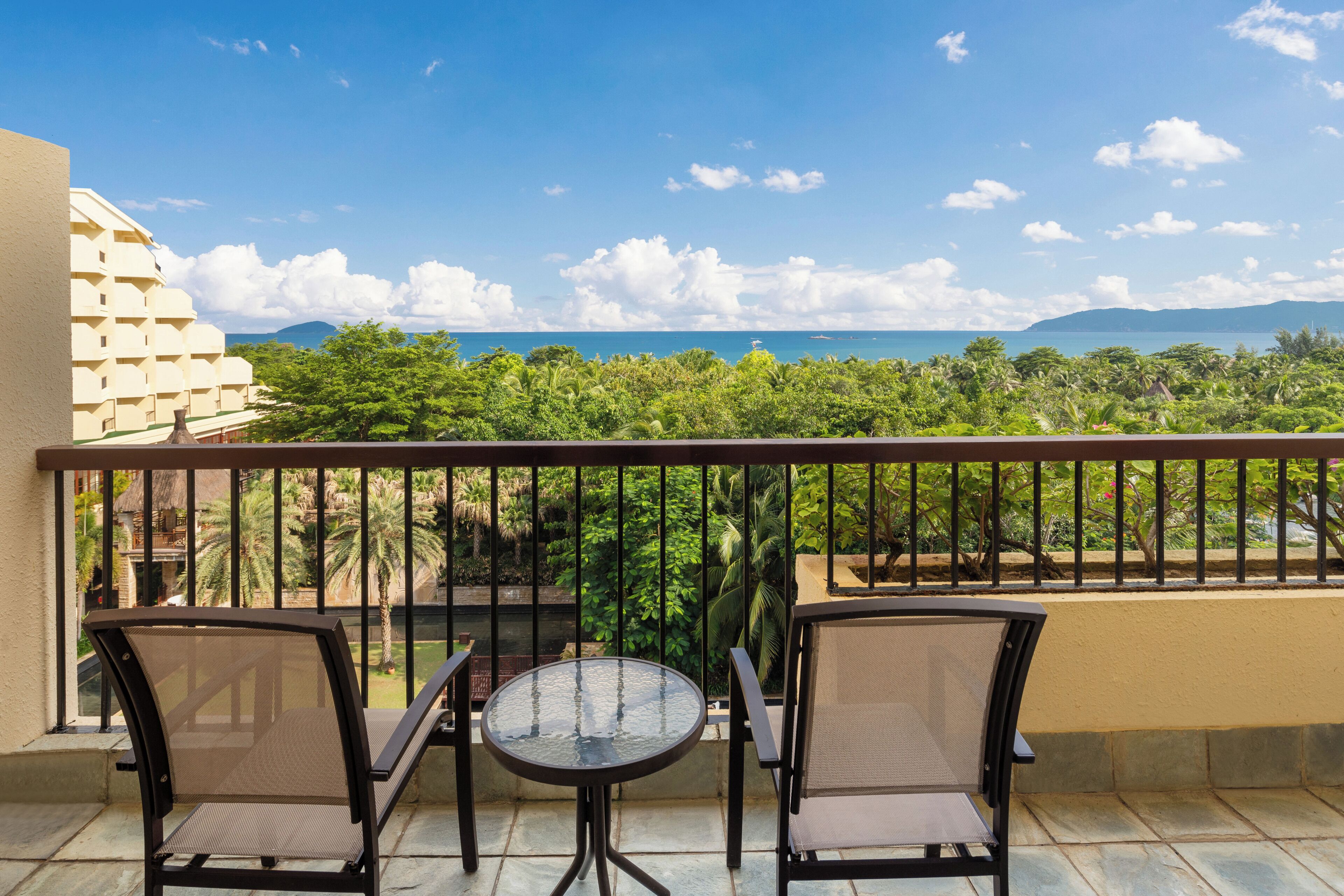 A balcony with two chairs and a small table, overlooking a lush landscape and a distant mountain range.
