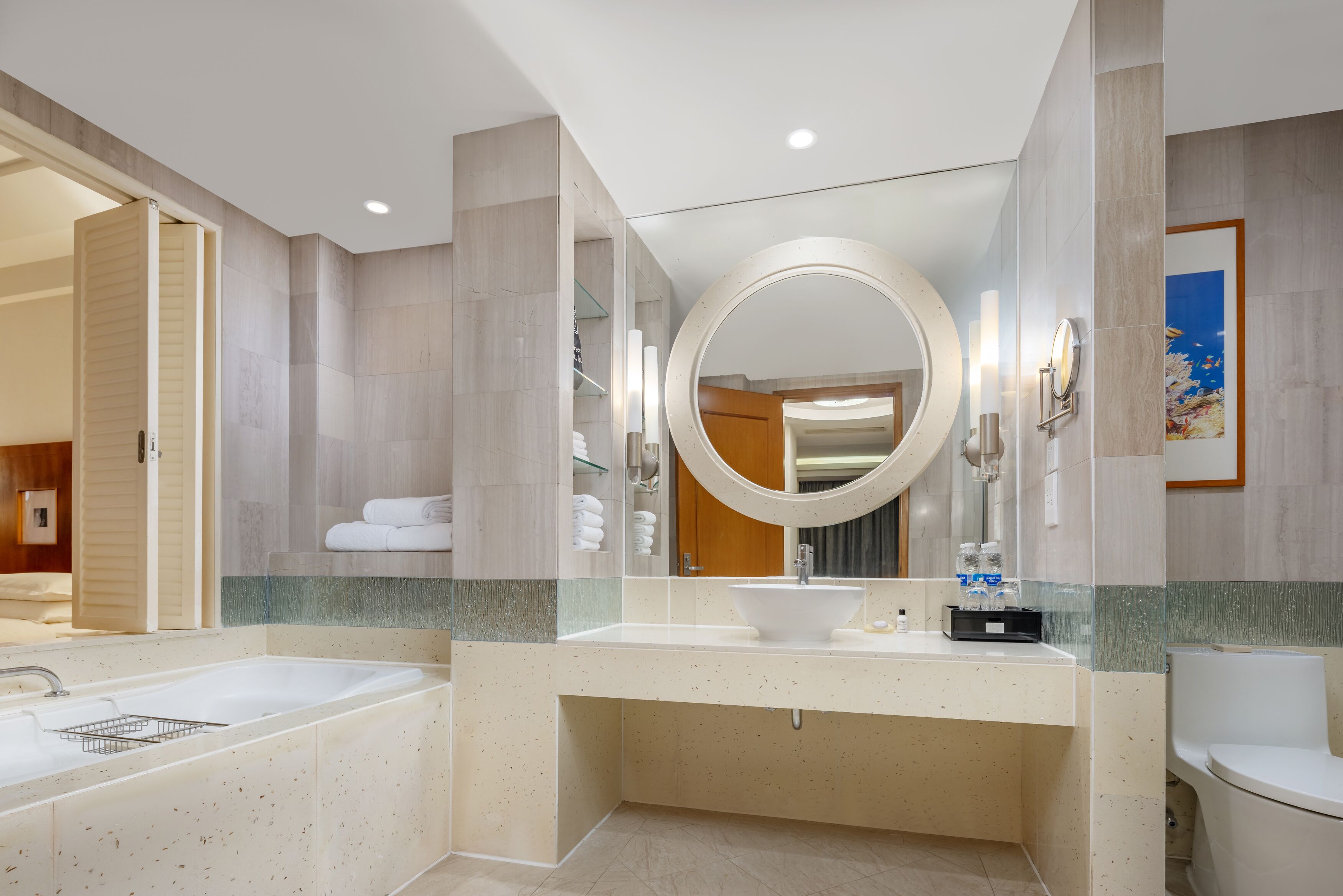 A modern bathroom with a large oval mirror, dual sinks, and a bathtub.