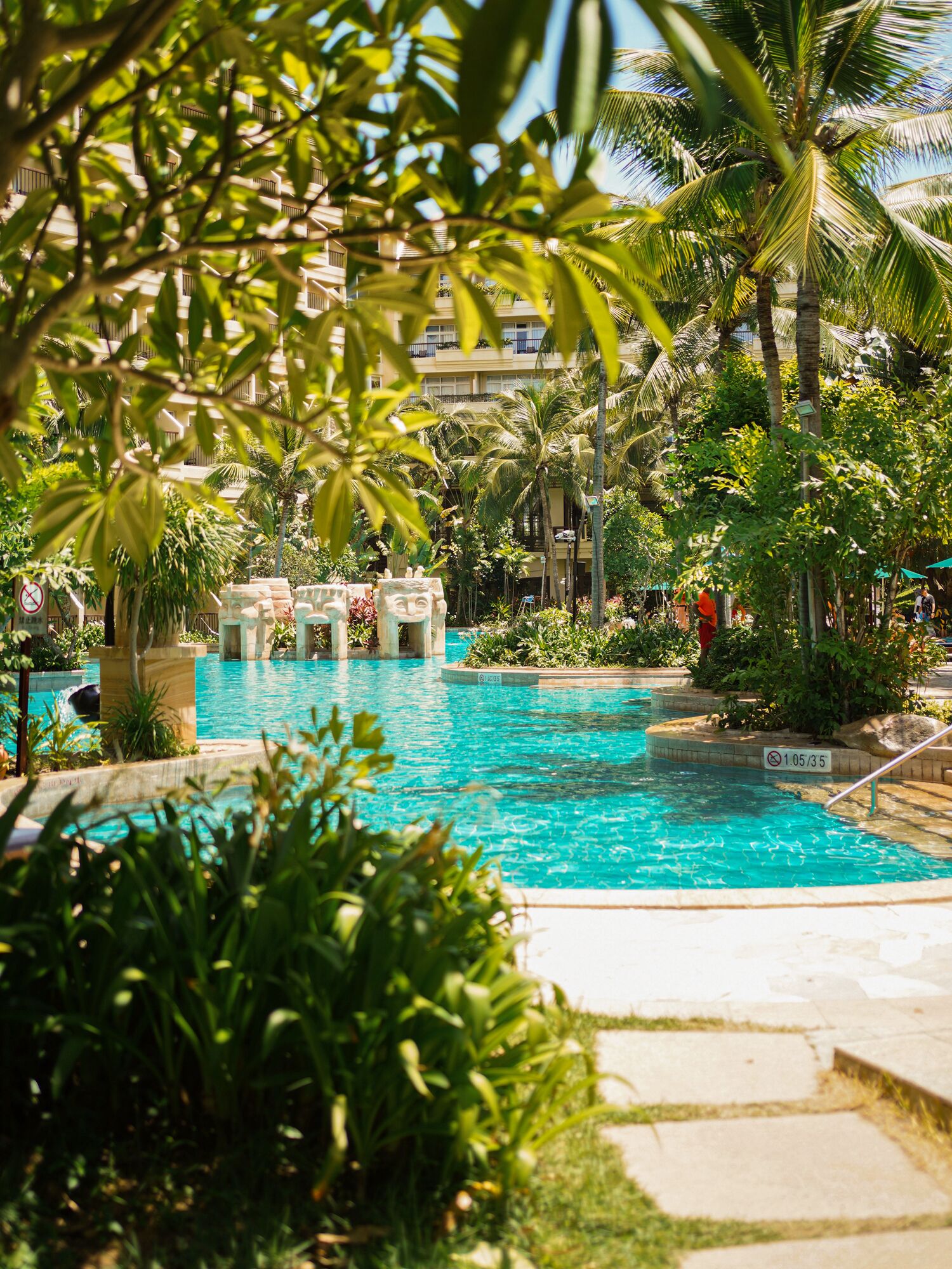 A swimming pool with clear blue water, surrounded by lush greenery and palm trees.