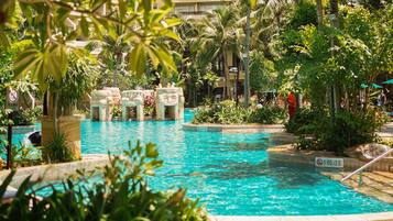 A swimming pool with clear blue water, surrounded by lush greenery and palm trees.
