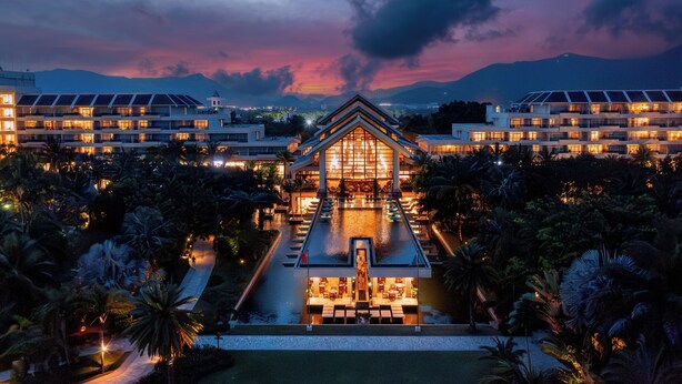 Un hotel con una estructura central de vidrio, varios pisos y un área de piscina circundante.