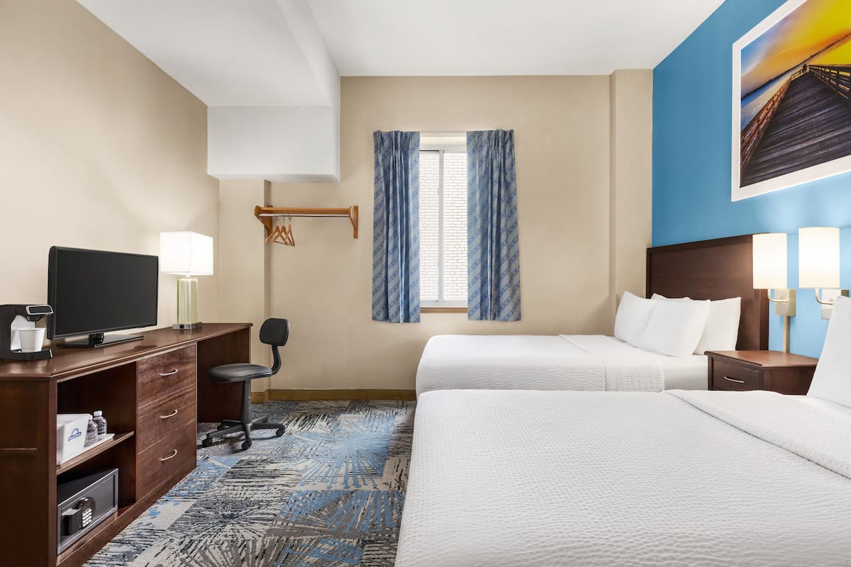 A hotel room with a bed, a desk with a television, a chair, a desk lamp, and a window with curtains.