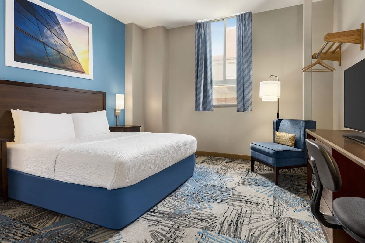 A hotel room with a large bed, a desk with a chair, a TV, and a window with curtains.