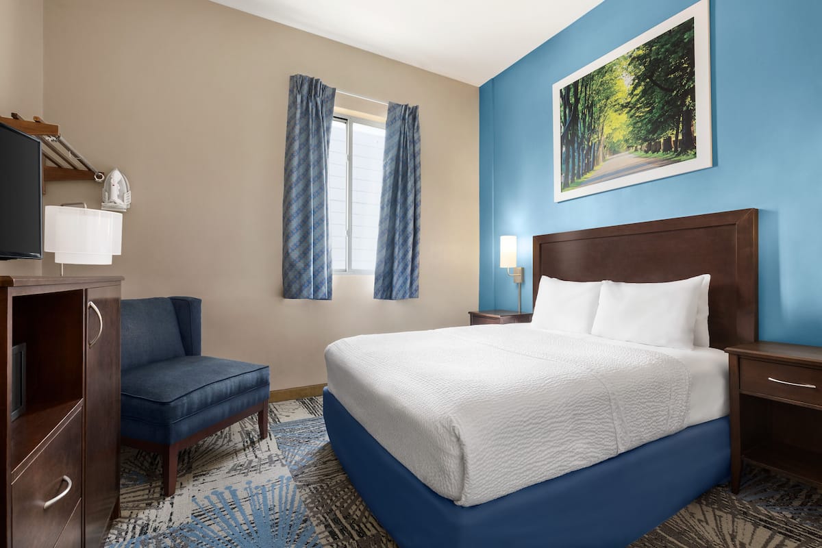 A hotel room with a large bed, a desk, a chair, a TV, and a painting on the wall.