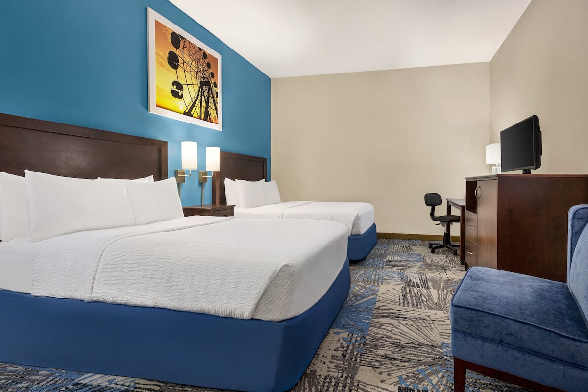 A hotel room with two beds, a desk, a chair, and a television.
