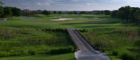 A golf course with a long, straight pathway leading to a water hazard, surrounded by lush green grass and trees.