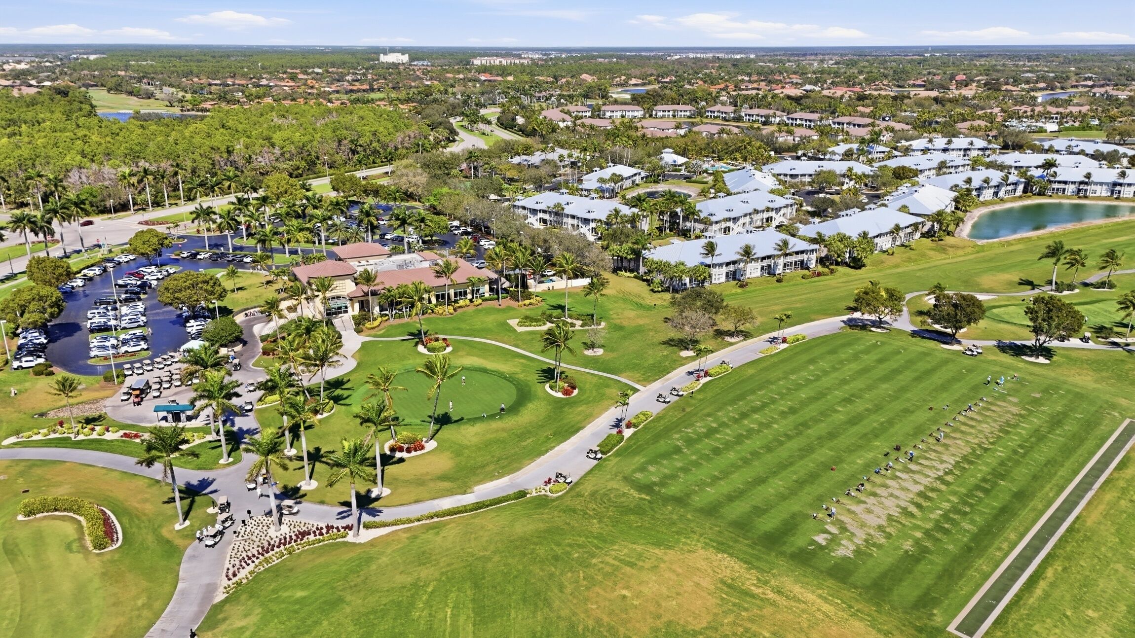 An aerial view of a golf course with a clubhouse, parking areas, and residential buildings.