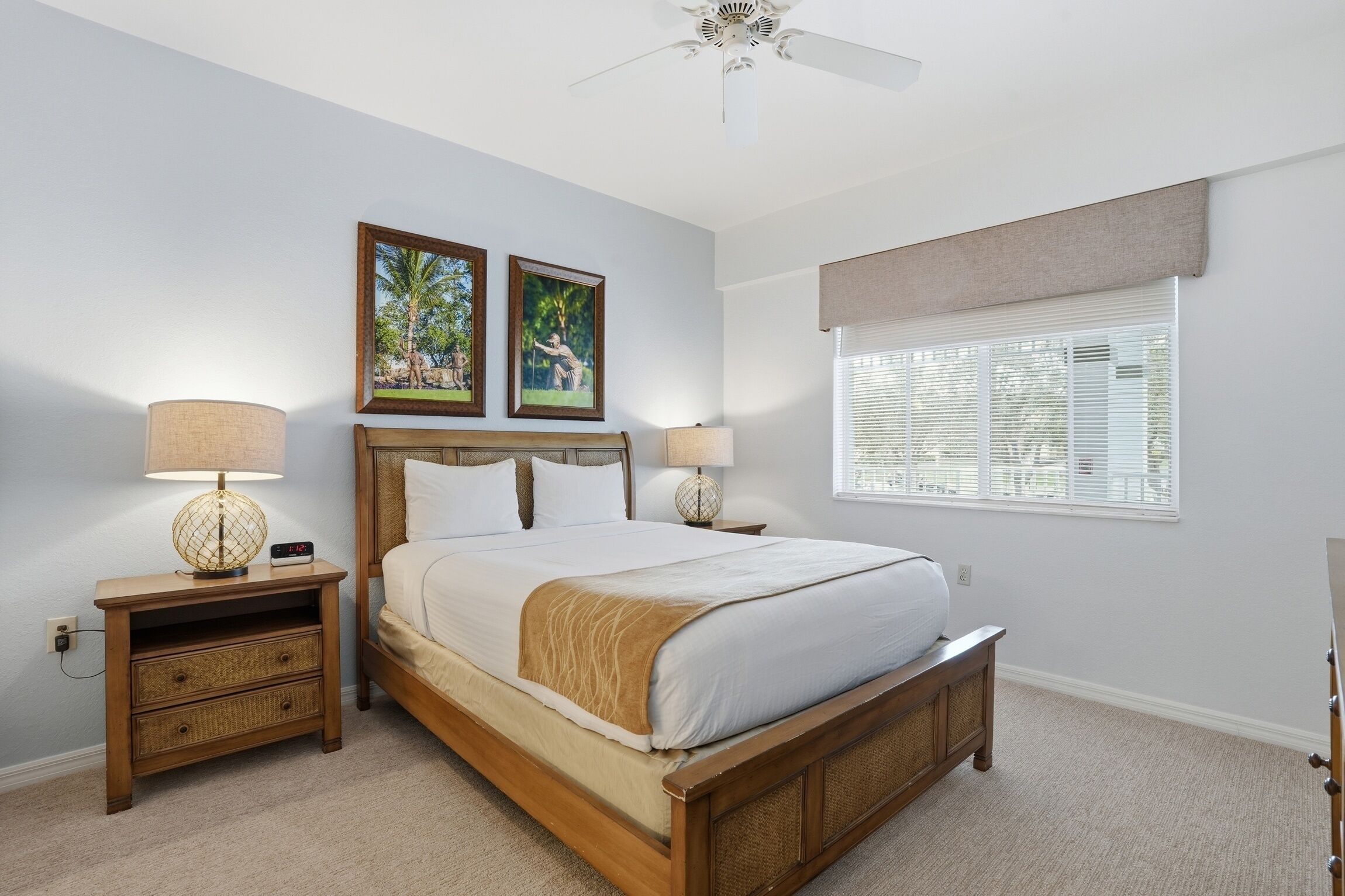 A bedroom with a bed, two bedside tables, a lamp, a ceiling fan, and a window with blinds.