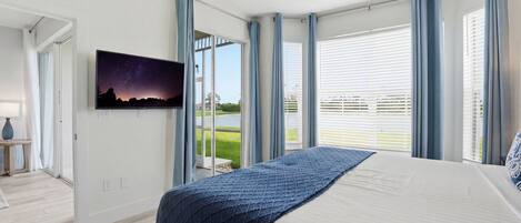 Quarto com cama grande, televisão na parede e porta de vidro deslizante para uma varanda.