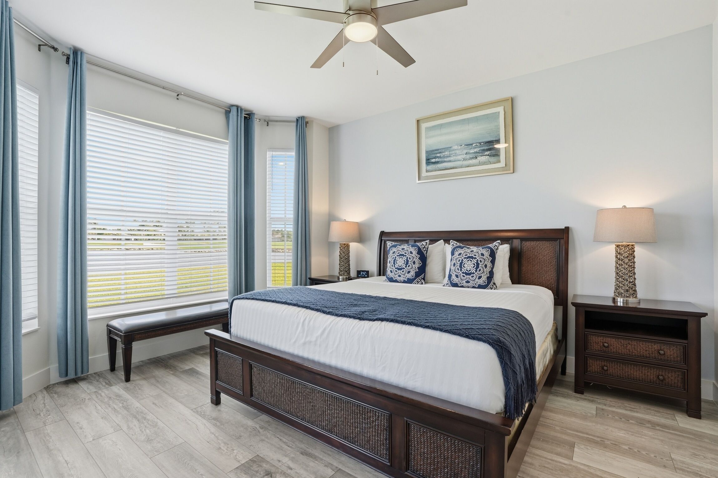 A bedroom with a bed, a bench, a ceiling fan, a nightstand, and a window with curtains.