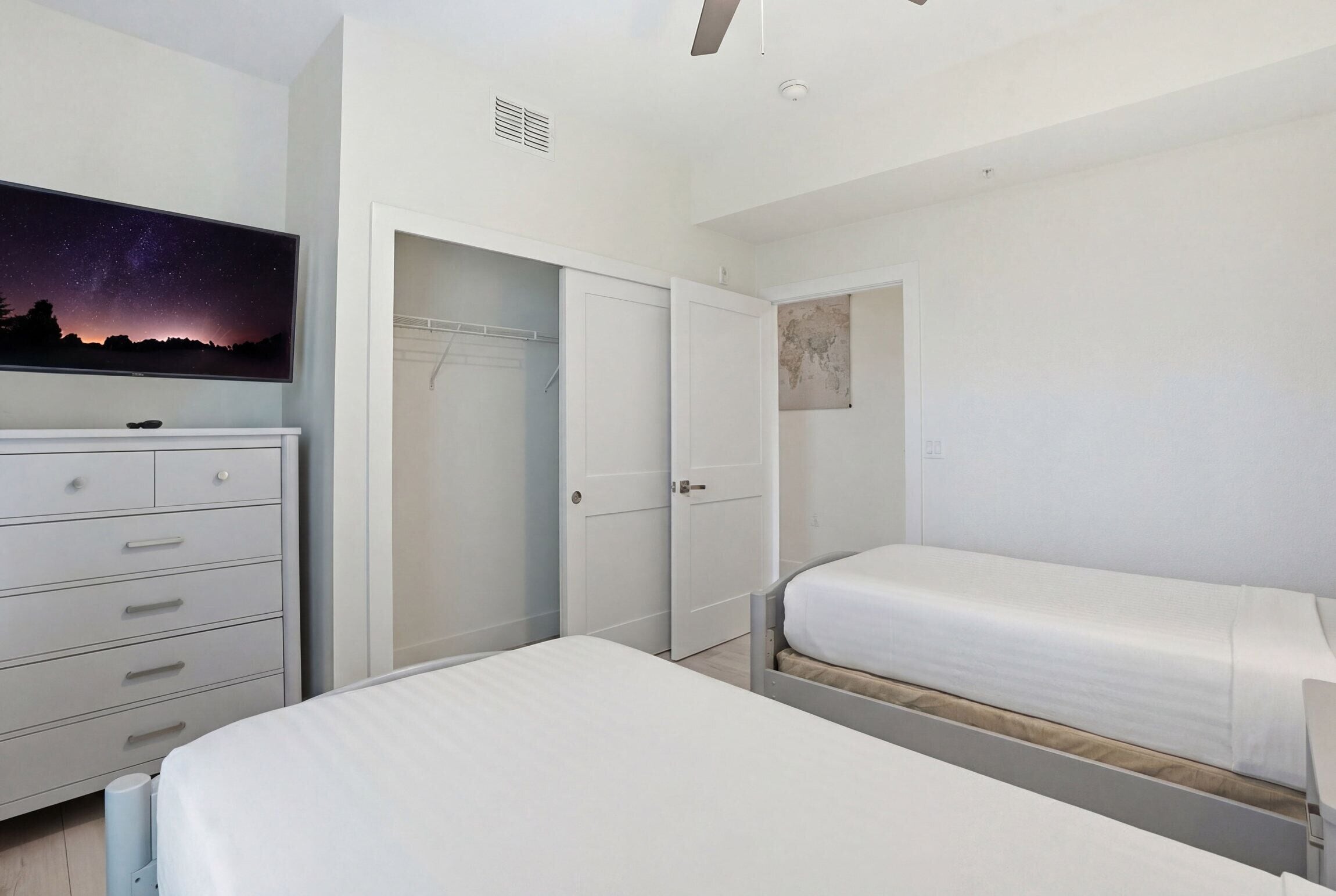 A bedroom with a bed, a dresser, a wardrobe, and a wall-mounted TV.