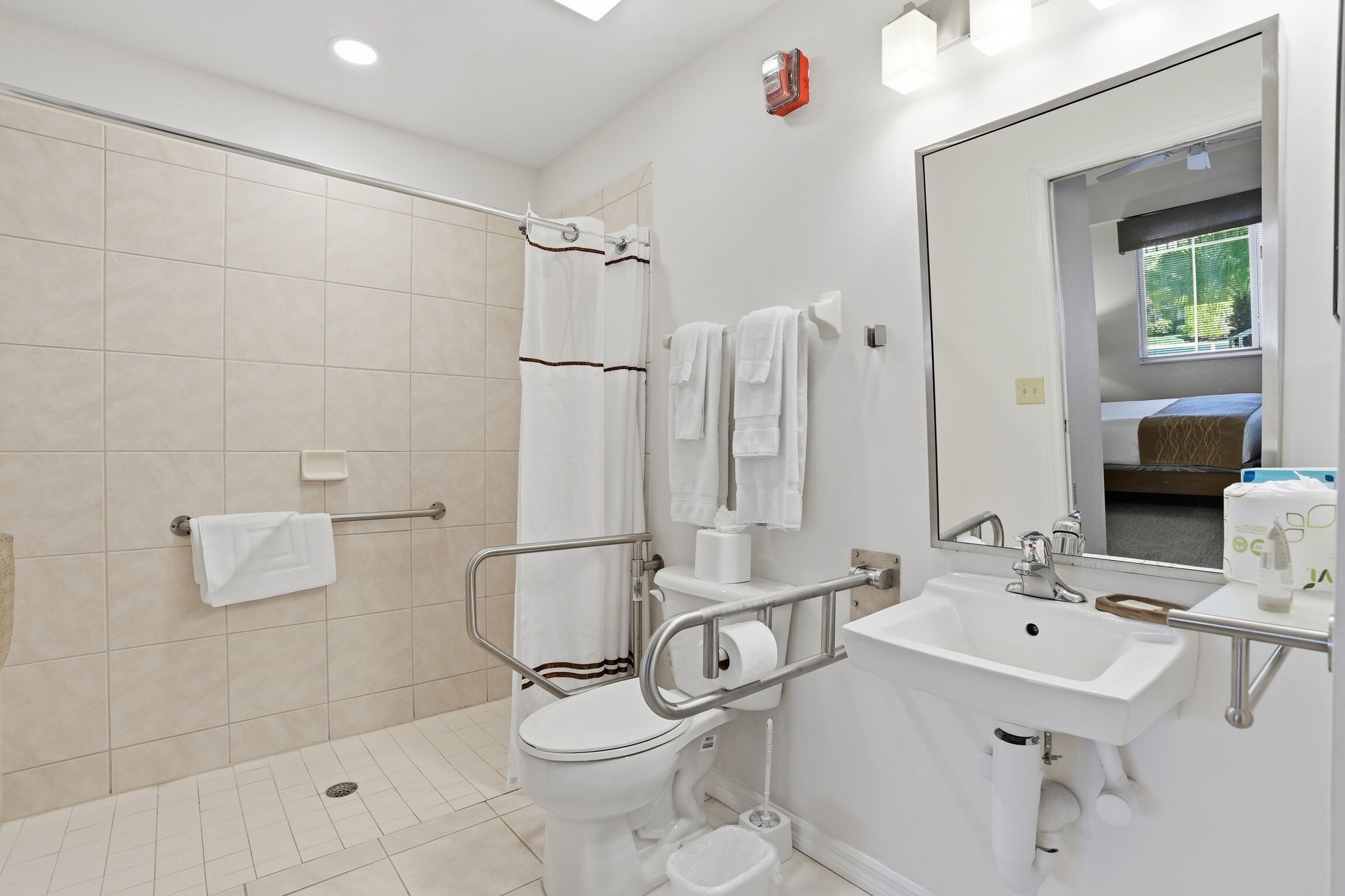 A bathroom with a shower, toilet, and sink, equipped with grab bars and a handrail.