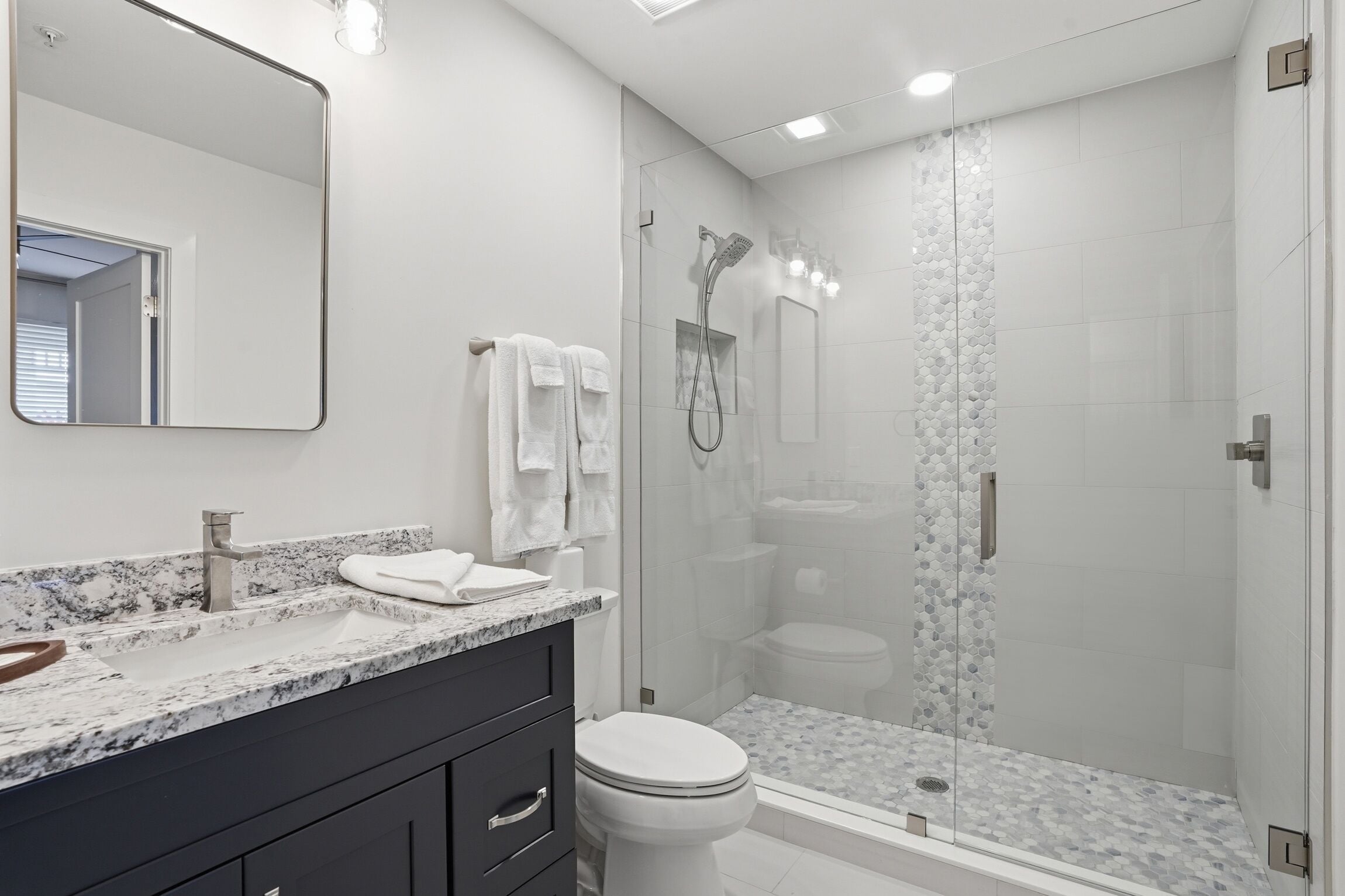 Un baño moderno con ducha envuelta en vidrio, inodoro blanco y encimera de mármol.