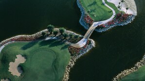 Vista aérea de un campo de golf con varias masas de agua, búnkeres de arena y un puente que conecta diferentes zonas.