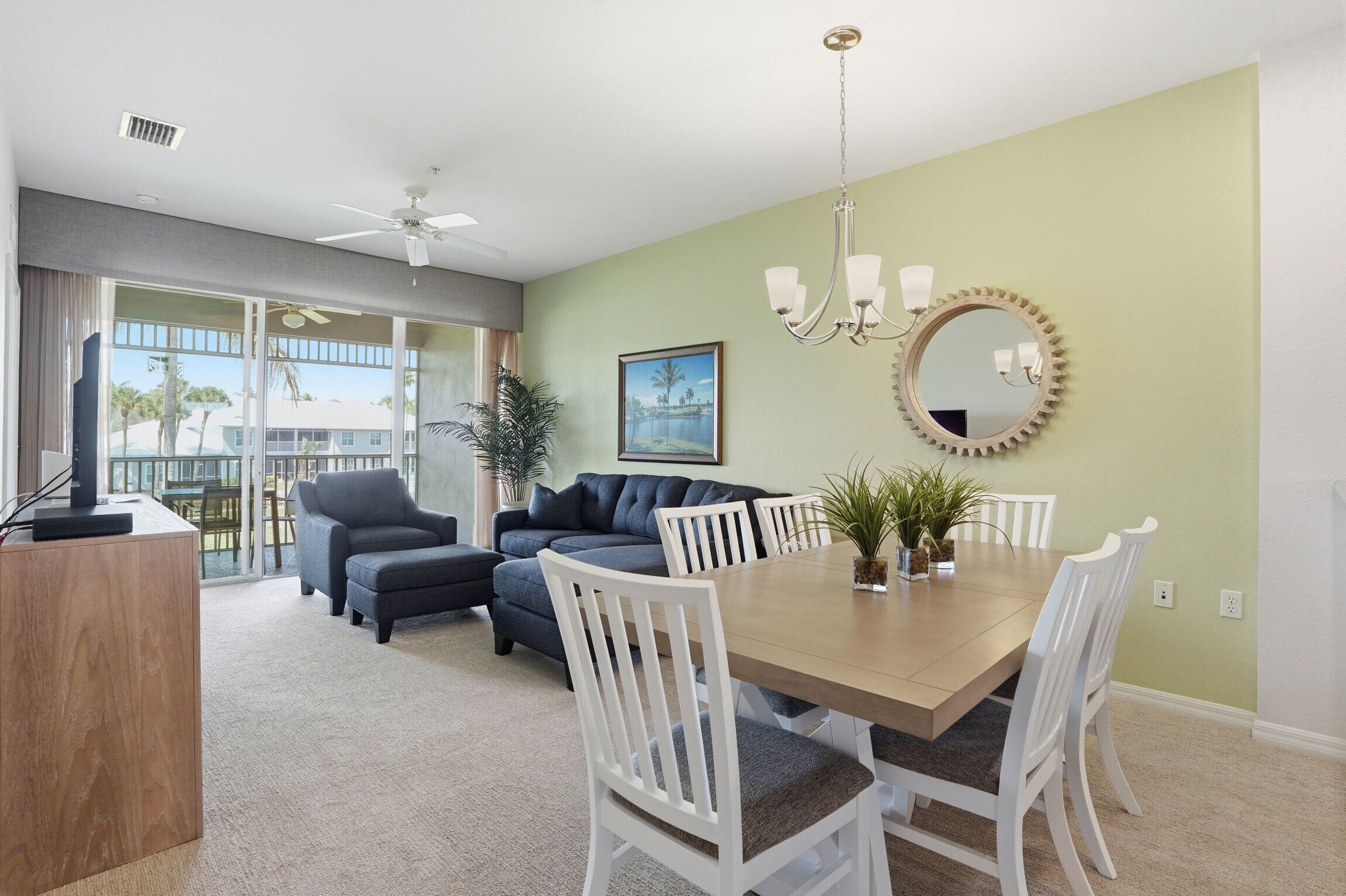 A dining area with a table, chairs, a chandelier, a mirror, and a sofa.