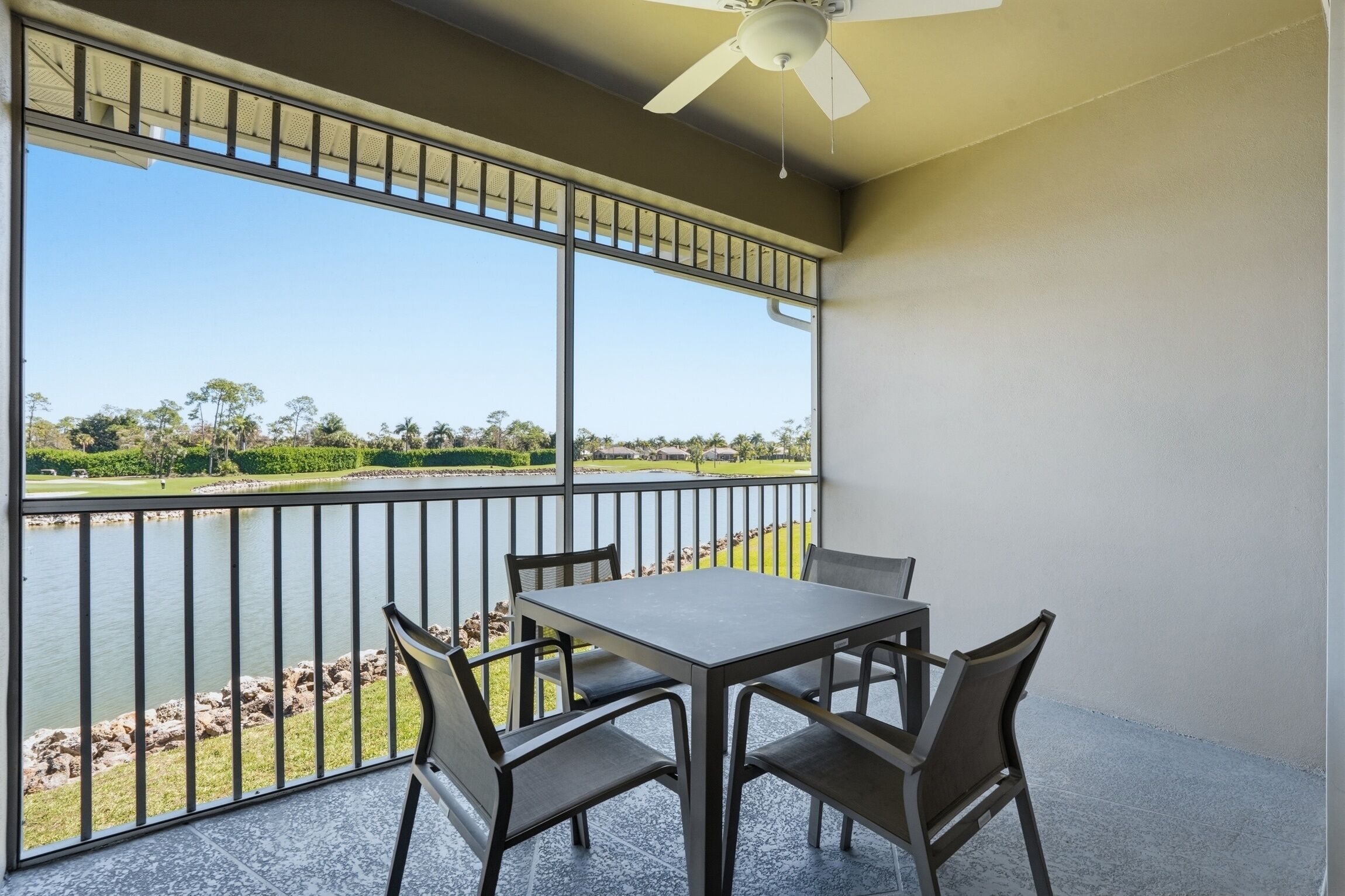 A balcony with a table and chairs, a ceiling fan, and a view of a lake and greenery.