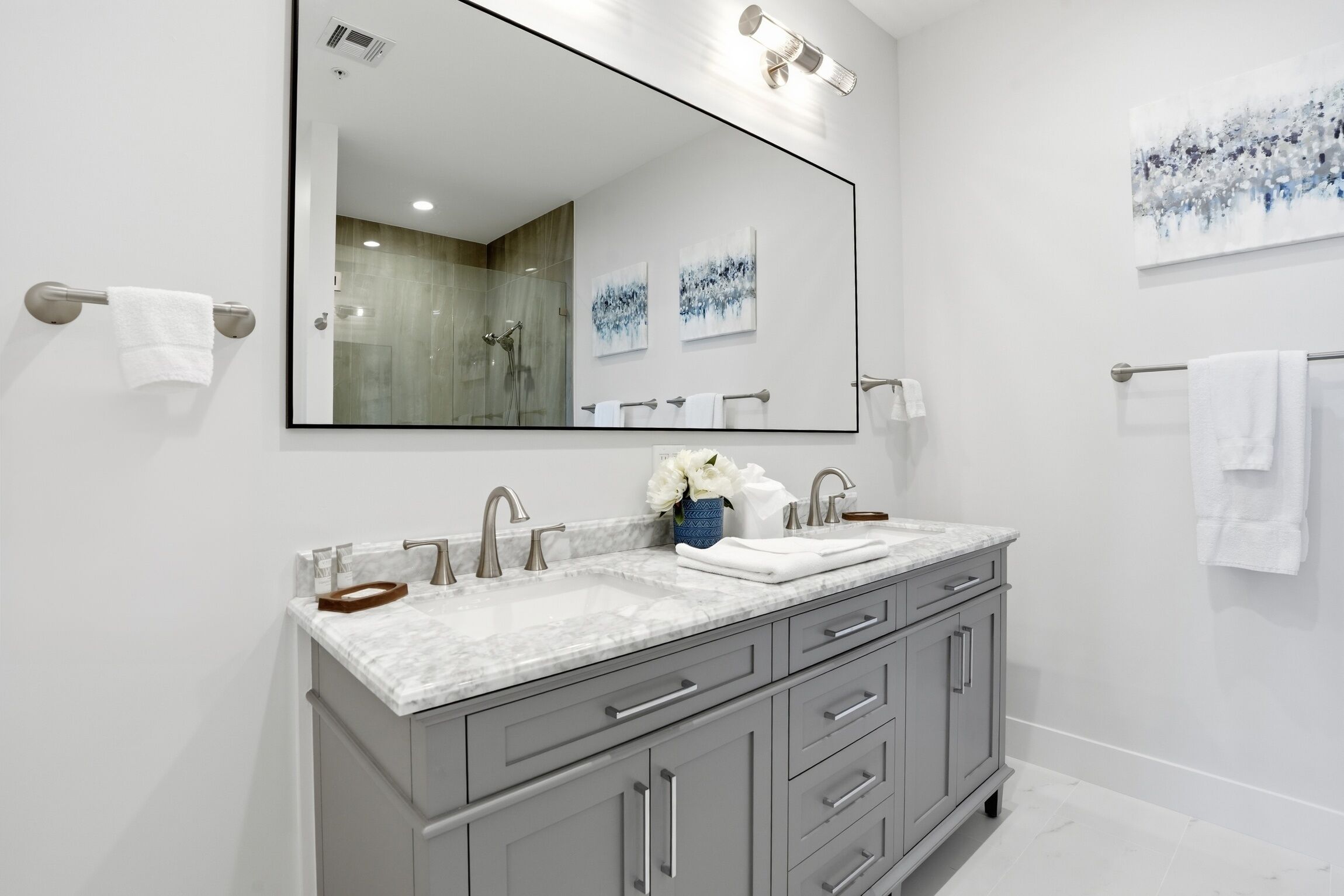 A modern bathroom with a large mirror, two sinks, grey cabinets, and white towels.