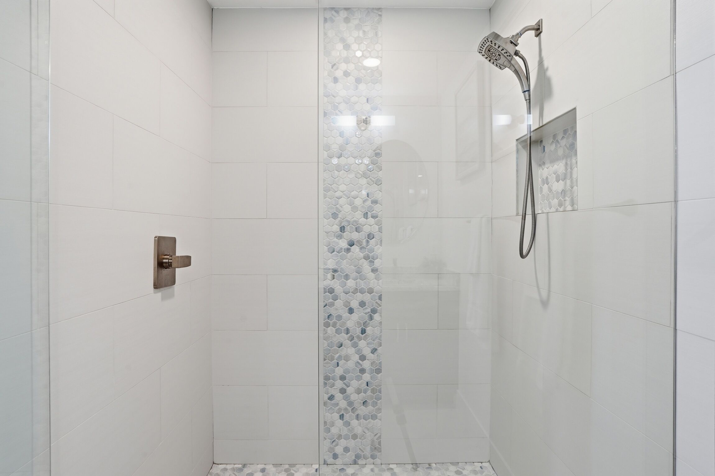 A shower with a glass door, a showerhead, and a control panel.