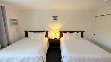 Habitación de hotel con dos camas individuales, una mesita de noche con lámpara, un aire acondicionado instalado en la pared y un cuadro enmarcado sobre las camas.