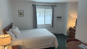 Une chambre d’hôtel comprenant un lit, une table de chevet, une lampe, un bureau, une chaise et une fenêtre avec des rideaux.