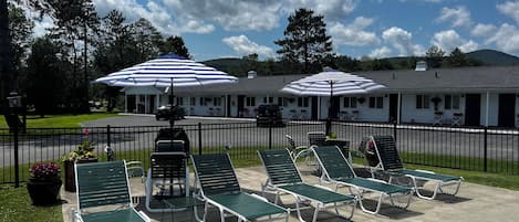 A motel with outdoor lounge chairs and striped umbrellas, a parking lot, and a building with a white exterior.