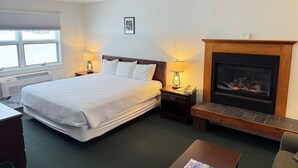 A hotel room with a large bed, a fireplace, a desk, and a chair. - Stowe Motel & Snowdrift (Stowe)