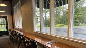 A bar area with a long counter, several chairs, and large windows offering a view of the outdoors. - Stowe Motel & Snowdrift (Stowe)
