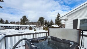 A hot tub in a snowy backyard with a wooden deck and a house in the background. - Stowe Motel & Snowdrift (Stowe)