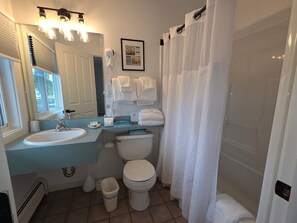 Une salle de bain avec un lavabo, des toilettes et un rideau de douche. Des serviettes sont accrochées au mur, et il y a un cadre photo.