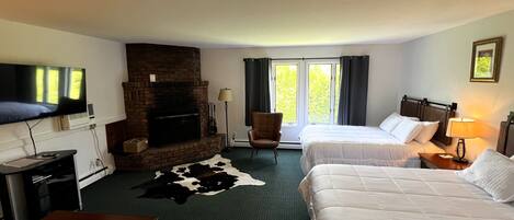 A hotel room with two beds, a fireplace, a TV, a desk, and a cowhide rug.