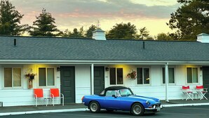 A blue convertible car parked in front of a white building with a porch, two red chairs, and a small table. - Stowe Motel & Snowdrift (Stowe)