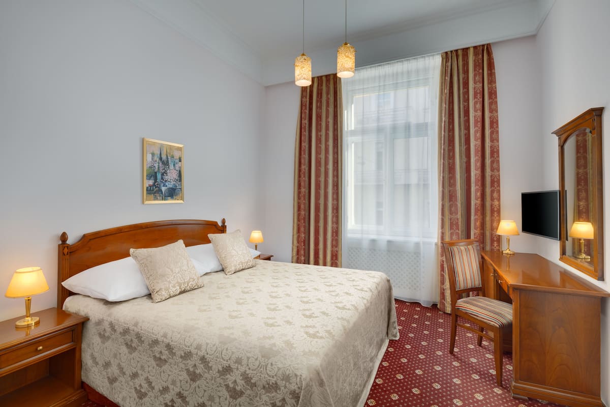 A hotel room with a wooden bed, a desk with a television, a chair, and a large window with curtains.