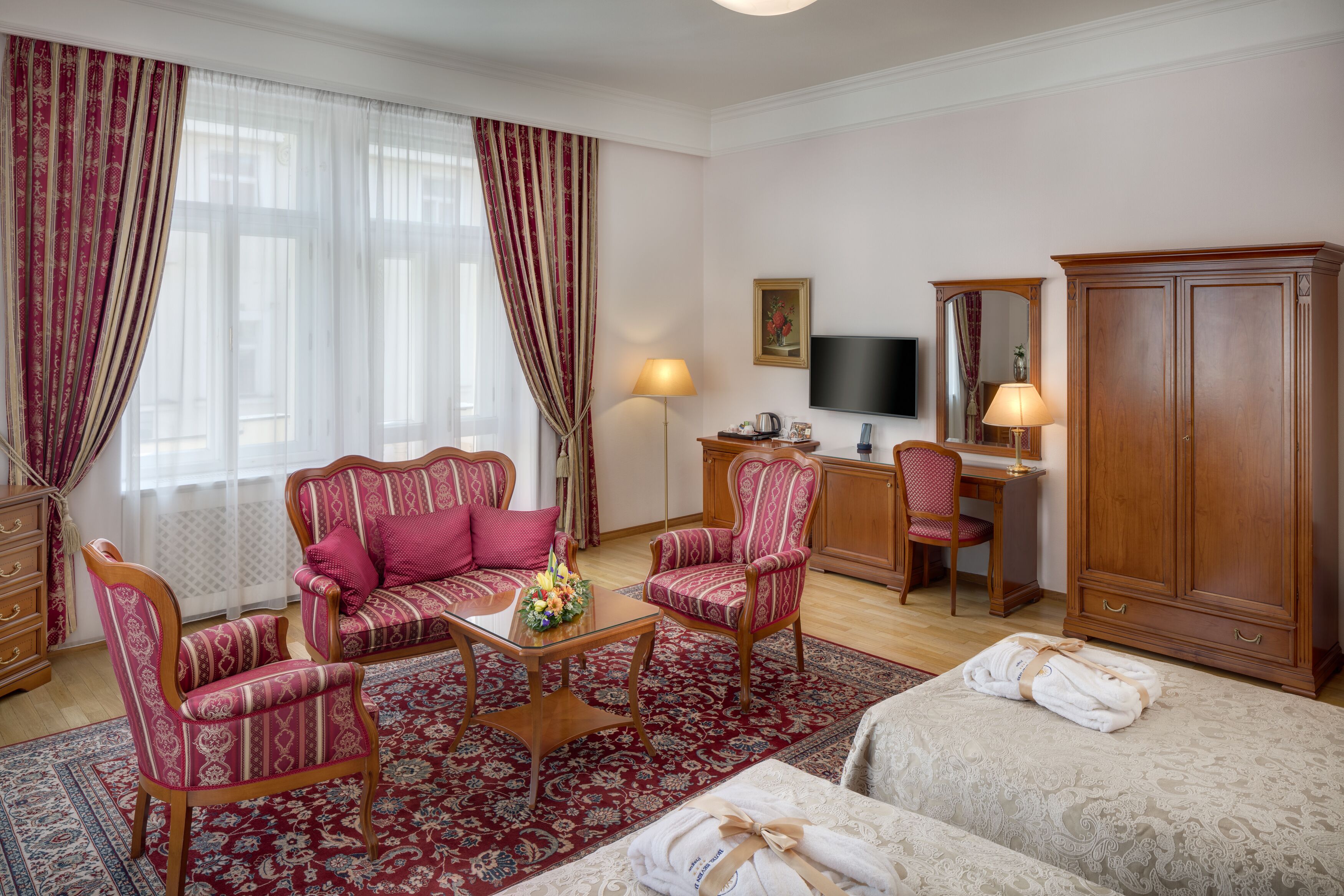 Quarto de hotel com sofá, poltronas, escrivaninha, televisão e guarda-roupa.