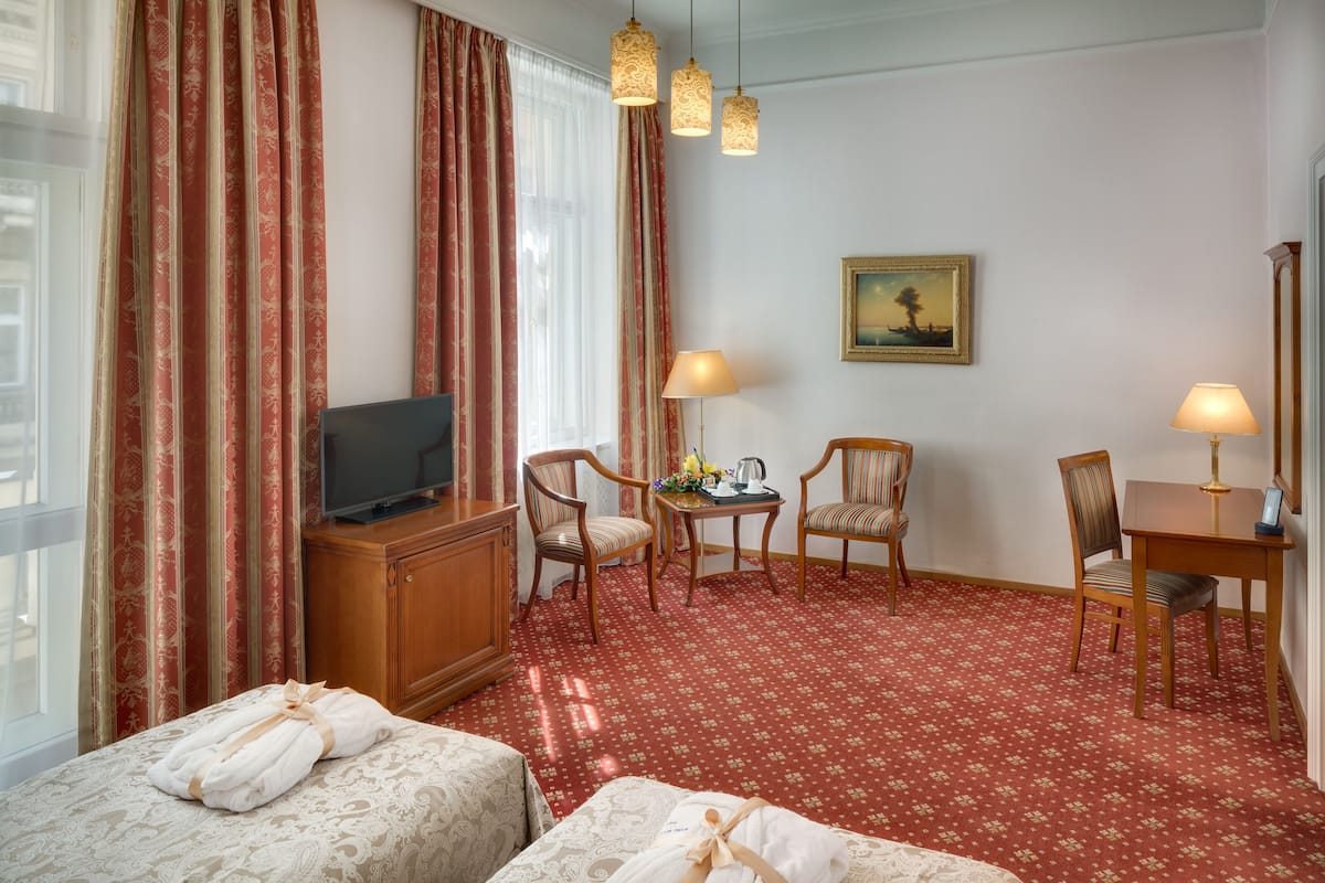A hotel room with a TV, two chairs, a small table, and a bed with towels.