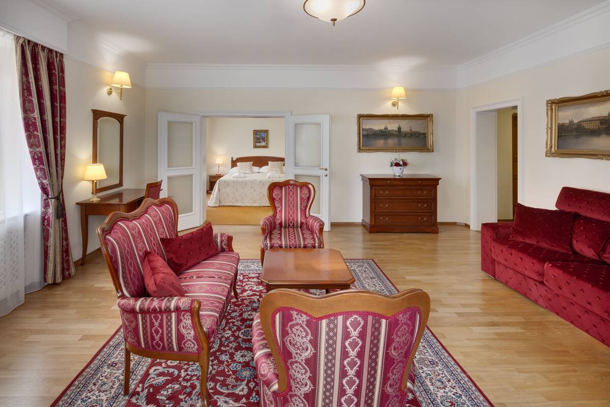 A hotel room with a bed, two armchairs, a sofa, a wooden coffee table, and a dresser.