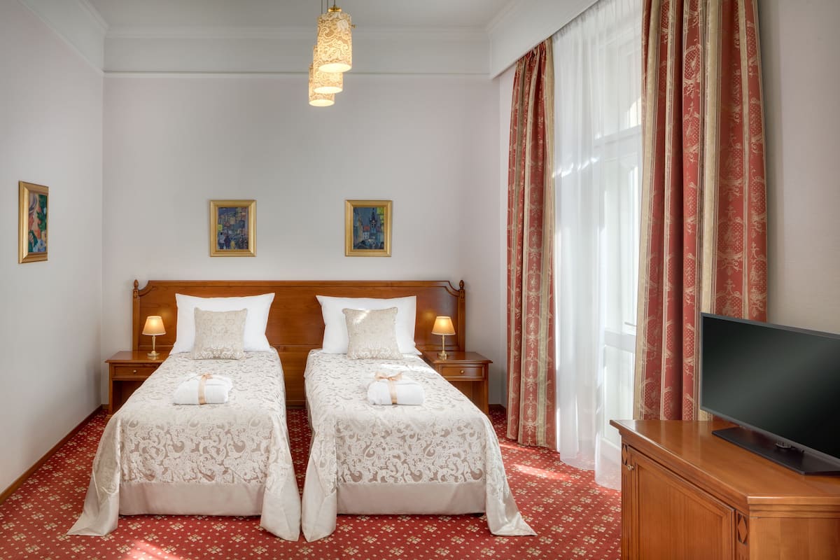 A double bed with a wooden headboard, two bedside tables with lamps, a flat-screen TV, and a red floral carpet.