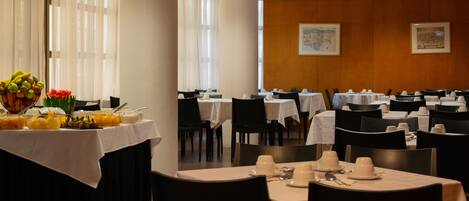 A dining area with multiple tables set for service, a fruit display, and framed artwork on the walls.