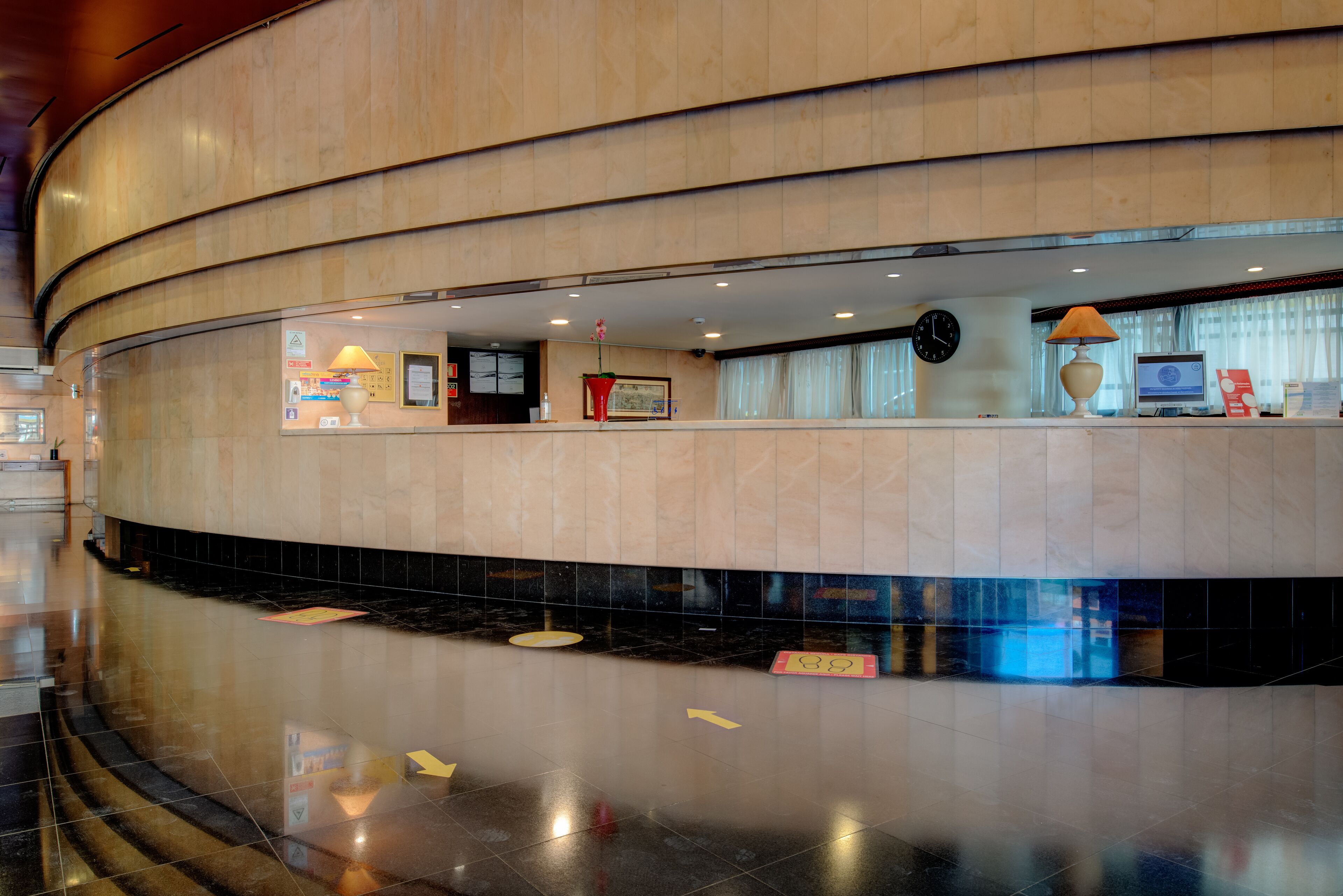 A hotel lobby with a curved reception desk, a clock, and a computer on the counter.