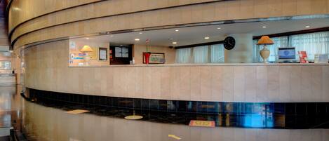 A hotel lobby with a curved reception desk, a clock, and a computer on the counter.