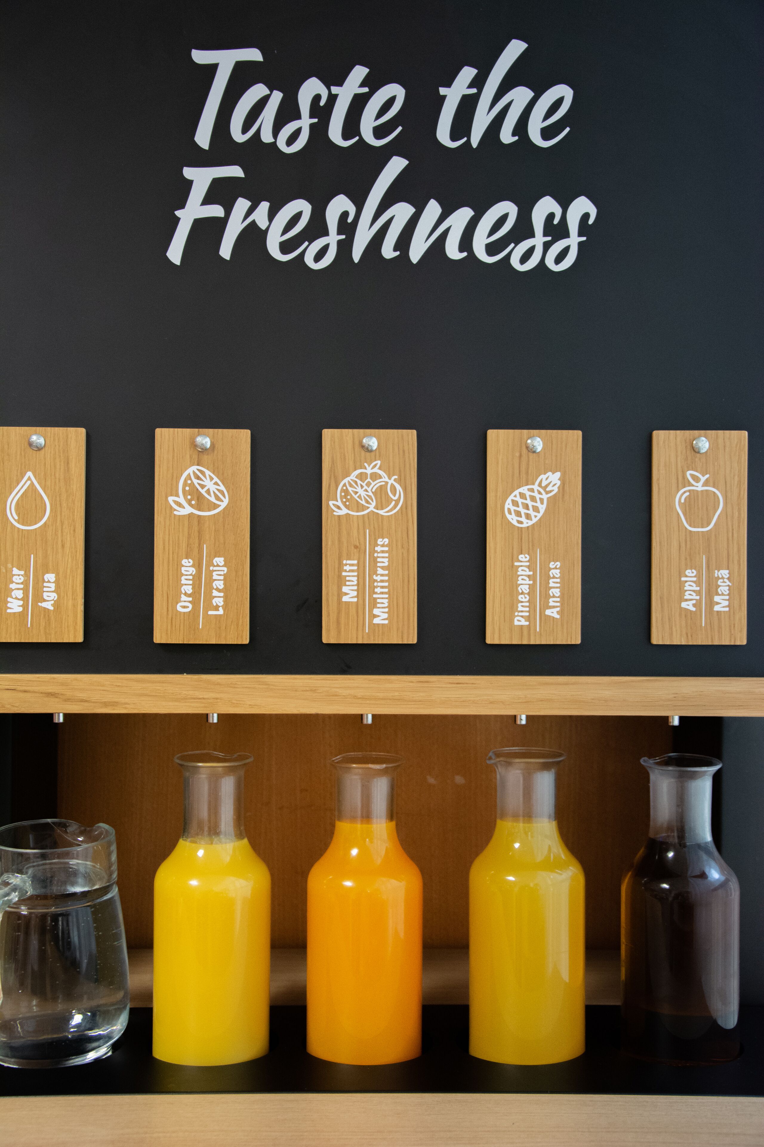 A wall with wooden labels indicating different types of water and juice, and a sign that says "Taste the Freshness".