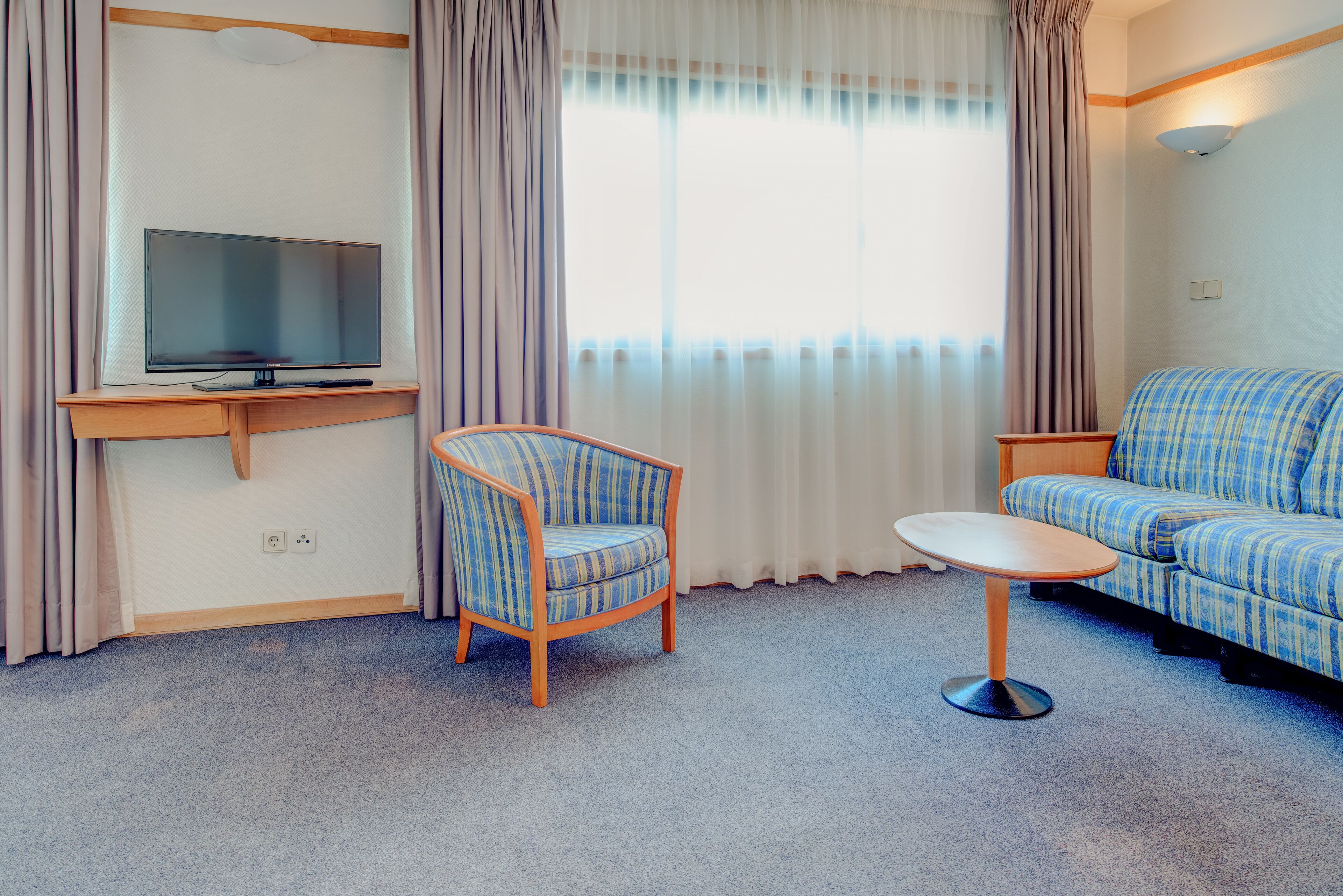 A living room with a television, a blue-striped armchair, a sofa, and a small table.
